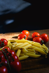 Fresh cherry tomatoes and raw pasta on wooden table with sunlight