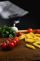Cherry tomatoes near raw pasta and garlic on wooden table and black background 
