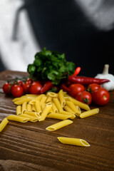Uncooked pasta and fresh vegetables on wooden table and black background 