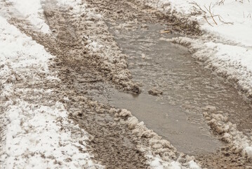 part of the road in white snow with brown mud and a gray puddle on a winter street