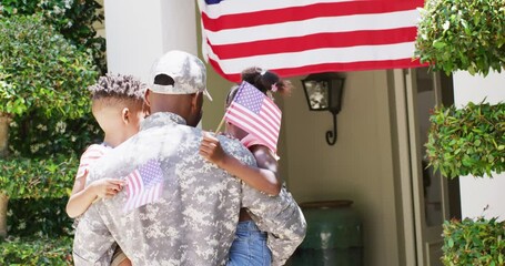 Happy african american male soldier returning home, holding son and daughter with flags, slow motion