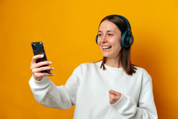 Laughing woman is watching a comedy over the phone while wearing headphones.