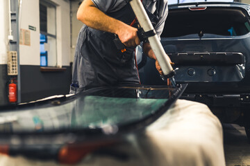 Mechanic adding glue to the windscreen of a car windshield replacement station. High-quality photo. - obrazy, fototapety, plakaty