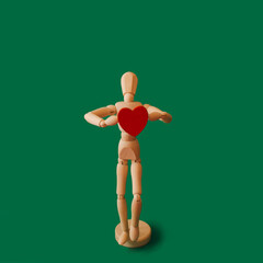 Wooden man with a heart in his hands on a green background