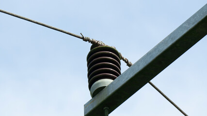 A close-up of a high-voltage electrical insulator and wire on a power pole against a clear sky,...