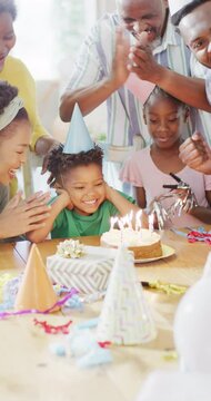 Vertical video of african american family birthday, son blowing out candles on cake, slow motion