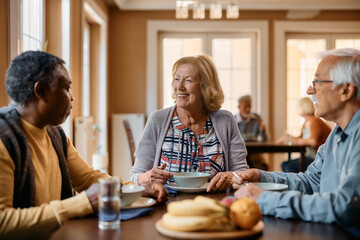 Happy senior woman and her friends communicating during meal at residential care home.