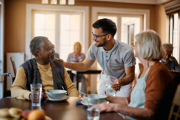 Fototapeta na wymiar Happy senior people and caregiver talk in dining room at nursing home.