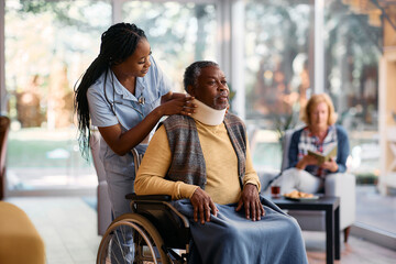 Young black nurse putting cervical collar on senior man's neck at nursing home.
