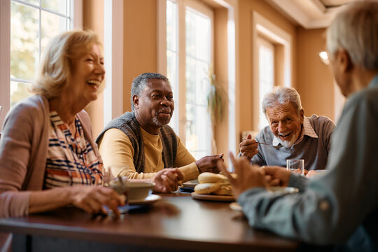 Group of cheerful senior people enjoy in conversation during lunch at nursing home.