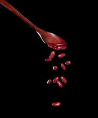 Red Bean fall, red grain beans explode abstract cloud fly from wooden spoon. Beautiful complete seed pea bean, food object design. Selective focus freeze shot black background isolated