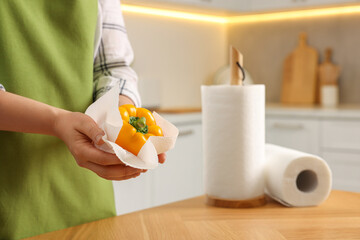 Woman wiping bell pepper with paper towel in kitchen, closeup. Space for text