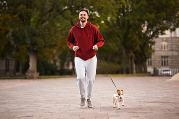 Obraz premium Man running with adorable Jack Russell Terrier on city street. Dog walking