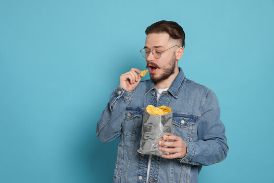 Handsome Young Man Eating Tasty Potato Chips On Light Blue Background