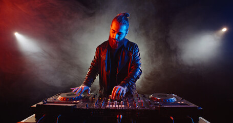 Authentic hipster dj rocking the party up. Bearded disc jockey working in a nightclub, composing a...