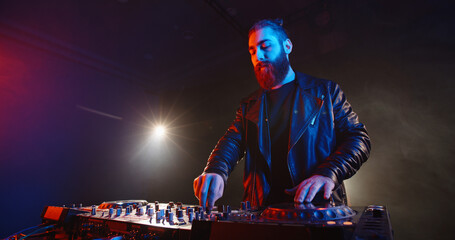Cool bearded disc jockey working at mixer controller in a nightclub. Authentic dj performing in...