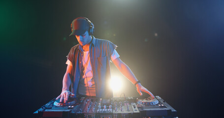 A cool young dj approaches the mixer controller and puts headphones on, ready to perform in a...