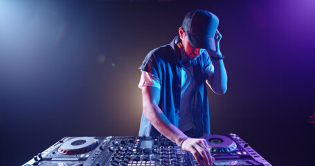 Cool hipster disc jockey performing in a nightclub at a mixer controller, spotted by colorful...