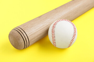 Wooden baseball bat and ball on yellow background, closeup. Sports equipment