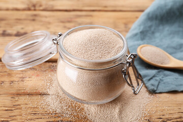Glass jar and spoon with active dry yeast on wooden table, closeup