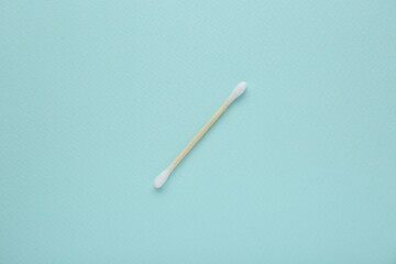 One wooden cotton bud on turquoise background, top view