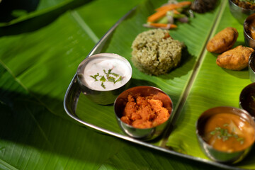 Yogurt, chutneys, sauces, and rice are served in small portions as an assorted meal plate on banana leaves, enjoyed at a south Indian restaurant.
