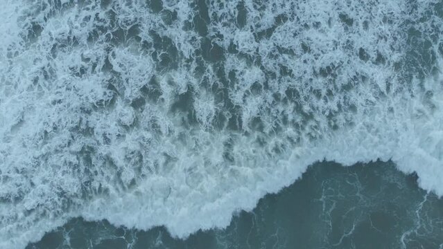 An overhead drone shot captures the textures of water as sea waves crush, foam, bubble, and swirl