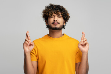 Indian man keeping fingers crossed, hoping his dream comes true, making cherished, gray background