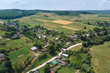 Aerial landscape view of village houses and distant green cultivated agricultural fields with growing crops on bright summer day