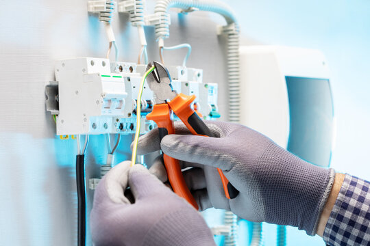 Electrician cuts electrical wires with pliers in electrical panel. Wire cutting process. Repair concept.