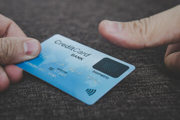 Close up of male hands holding credit card with fingerprint scanner and embedding the thumb to pay online. Concept of using biometric technology in banking. Cardholder touching his biometric card.