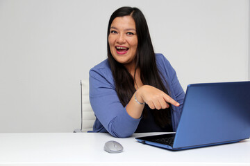 Latin adult woman works on her laptop in her office, celebrates and is amazed at a great achievement, success and triumph in her professional career
