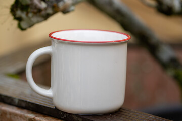 White mug, mock up, empty space for artwork, text, standing on stone, outdoors, green grass, trees, sky in the background, soft sunlight, nature