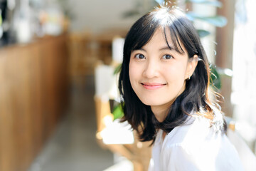 Brightly smiling beautiful young asian woman sitting in coffee cafe in sunny day