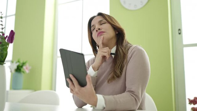 Young beautiful hispanic woman using touchpad with doubt expression at home