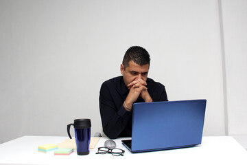 Dark-haired latin adult man works in his office with laptop with a lot of stress having a headache...