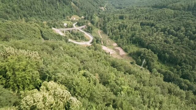 Dynamic flying with FPV racing drone close above the treetops. Descending fast towards an old old railway bridge and a winding road. Drone is flying under the bridge. LuPa Creative.