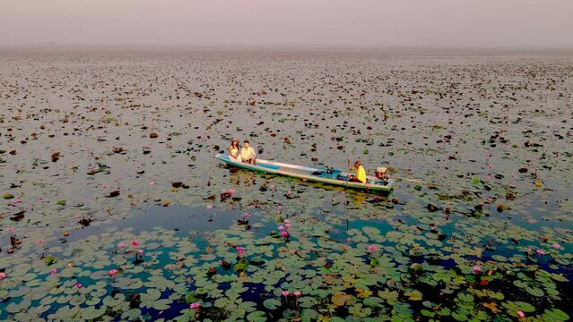 Sunrise at The sea of red lotus, Lake Nong Harn, Udon Thani, Thailand. Couple of men and women in a wooden boat during sunrise at the red lotus lake in Thailand