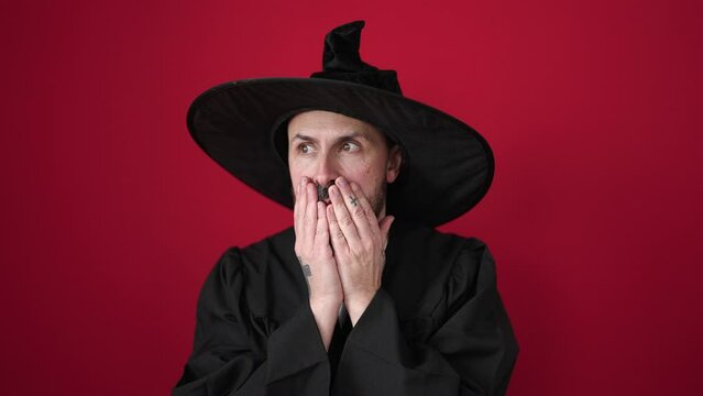 Young bald man wearing wizard costume standing with fear expression over isolated red background