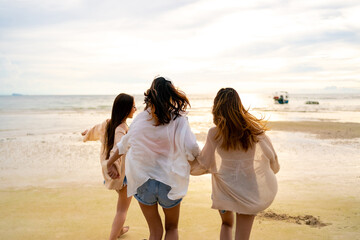 Group of Young Asian woman friends in walking and playing sea water together on tropical island beach at summer sunset. Attractive girl enjoy and fun outdoor lifestyle travel on beach holiday vacation