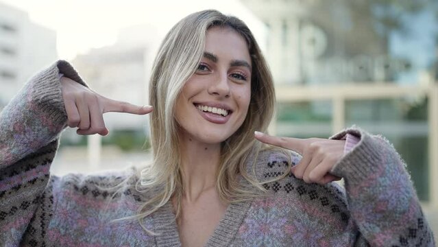 Young blonde woman smiling confident pointing with fingers to the mouth at street