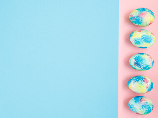 Colorful handmade Easter eggs painted like Earth on blue pink paper background with copy space for your Easter text message. Minimal happy Easter holiday conceprt. Top view flat lay, border frame