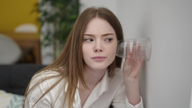 Young blonde woman spying neighbours with glass on wall at street