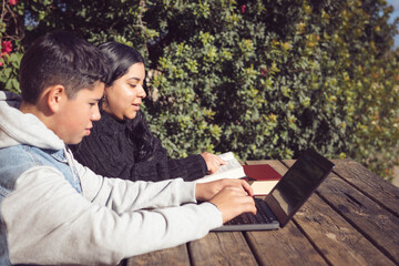 Fototapeta na wymiar two young Latino students, outdoors, using laptops, sitting at a park