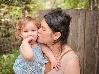 Mother kisses daughter on cheek, daughter looks at camera