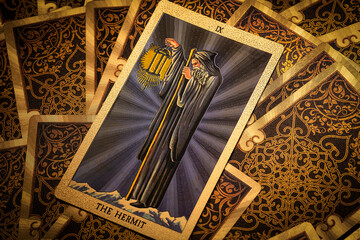 Gold embossed tarot cards on the table. The Major Arcana card The Hermit lies facing the viewer.