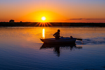 A wooden rowboat against an orange sunset with backlight in the twilight. Silhouette of a...