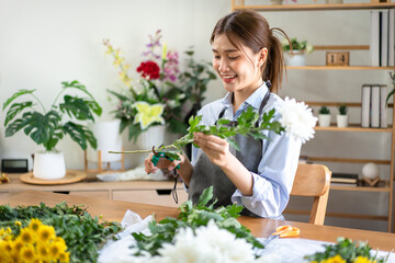 Female florist in apron using scissor to prepare and cutting ste