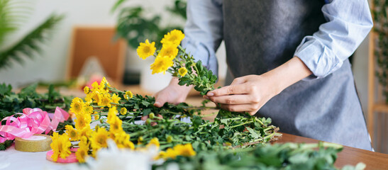 Female florist in apron selecting yellow chrysanthemum to creati
