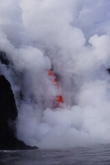 Hot stream of flowing lava surounded by white steam folling down from high cliff, Hawaii